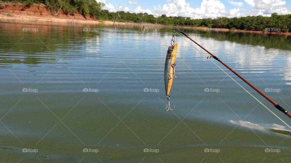 Peixinho artificial na ponta da vara sobre o rio, pronto para pescaria.