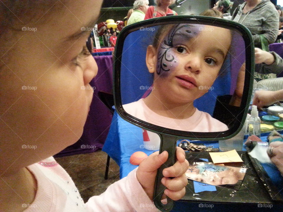 Girl looking in mirror with face paint on her face