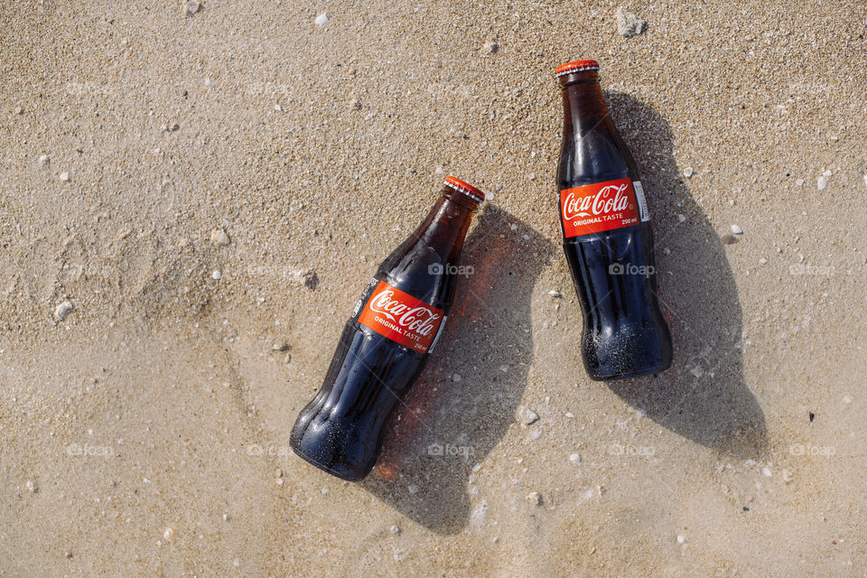 Two bottles of Coca-Cola on sandy beach