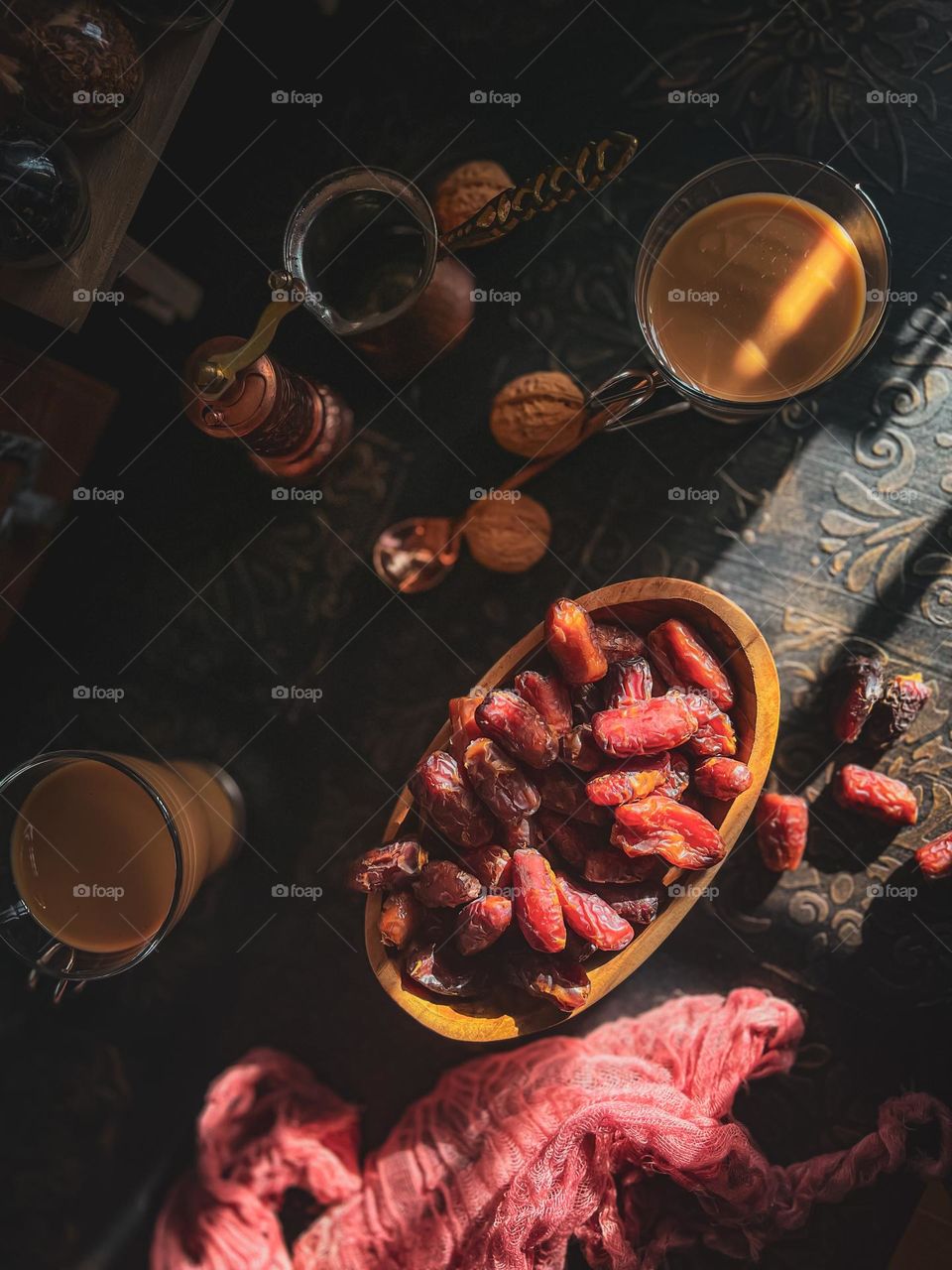 Top view of dried dates in a wooden bowl and textured table top with some hot milk tea on the table