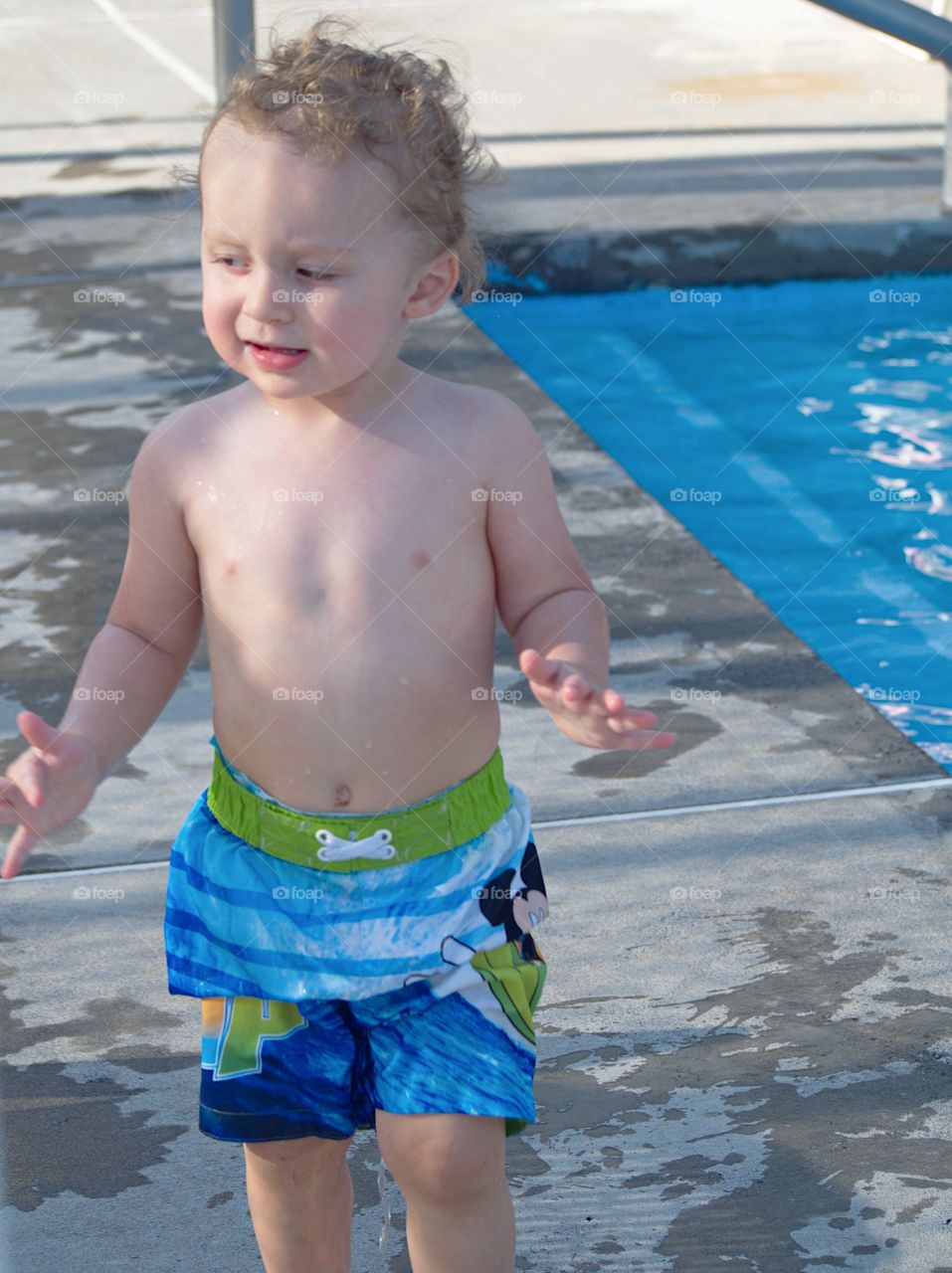 An unhappy toddler boy at the outdoor swimming pool for his first round of swimming lessons on a sunny summer evening. 