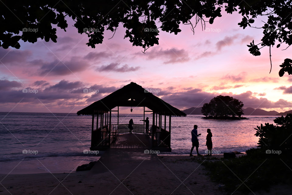 Sunset with people in beach hut framed by leaves