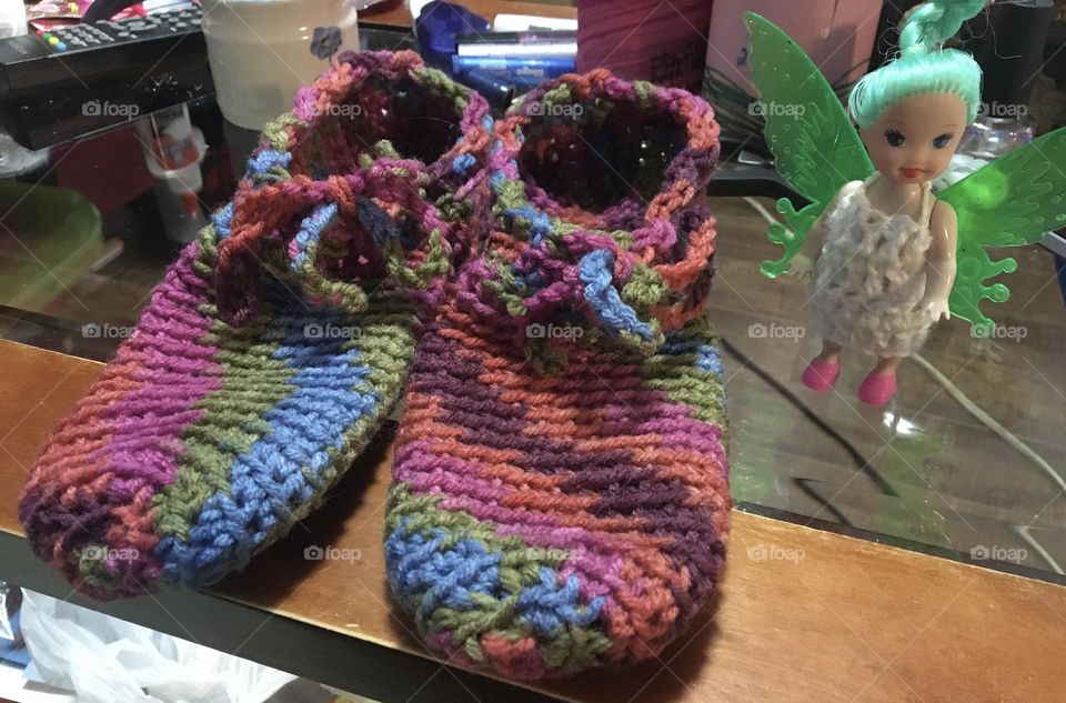 Some funky colourful handmade crocheted slippers, that I made for a friend that gave me this yarn, with pinks, browns, greens, blues, and purple variegated, sitting on my wood and glass coffee table