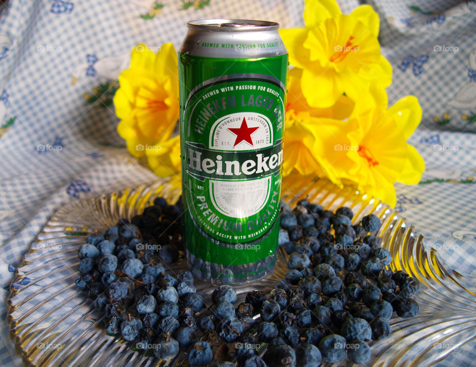 Heineken in glass dish and checkered tablecloth with yellow flowers, blue sloe, water drops.
