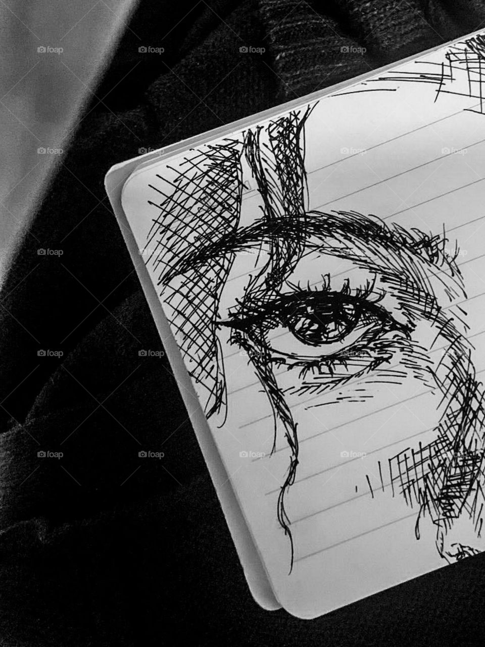 Black and white photo portrait showing sketches of eyes and parts of the face drawn in black ink on lined paper in a notebook