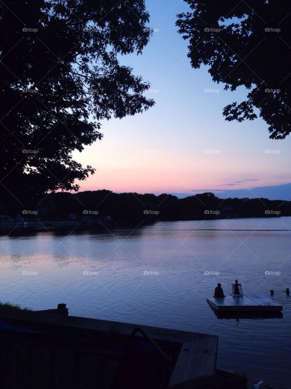 Summer evening sunset over a placid lake, surrounded by silhouetted trees and shoreline. (Lake Hiawatha, Bellingham, MA USA)