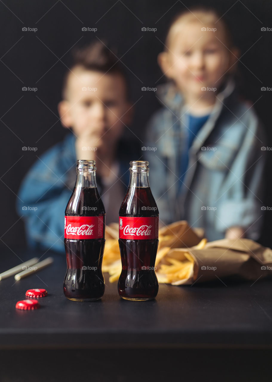 brother and sesira, stay at home, dressed in denim clothes, drink Coca-Cola from bottles through a straw.  beautiful stylish kids