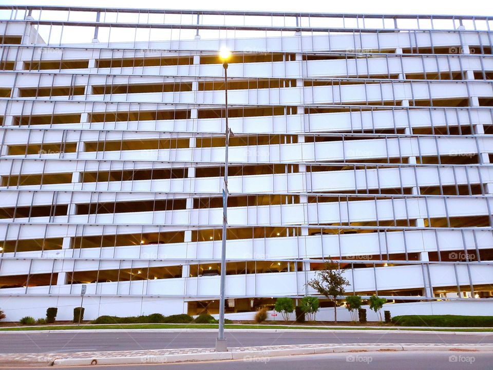 White cement multi-deck parking garage with exterior metal design and a metal post street light in the street median.