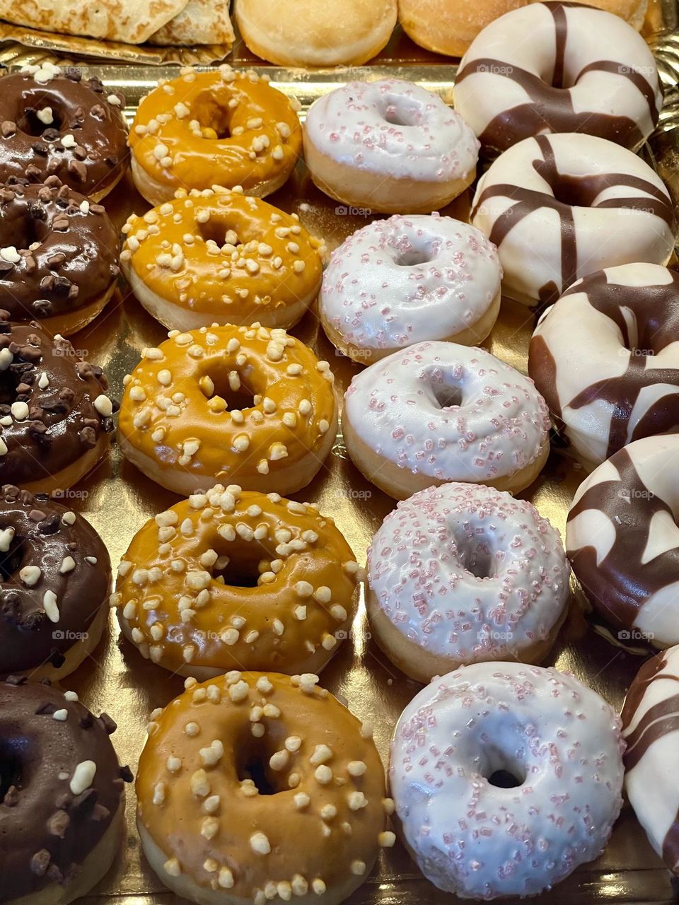 Colorful sugar and chocolate glazed donuts on golden serving platter from above 