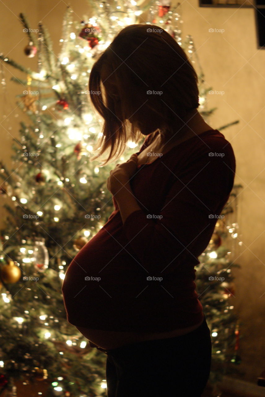 Side view of a pregnant woman standing near the illuminated christmas tree