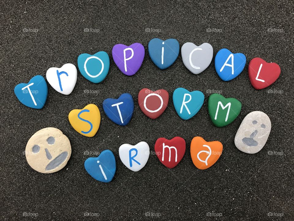 Tropical storm Irma text with colored heart stones over black volcanic sand