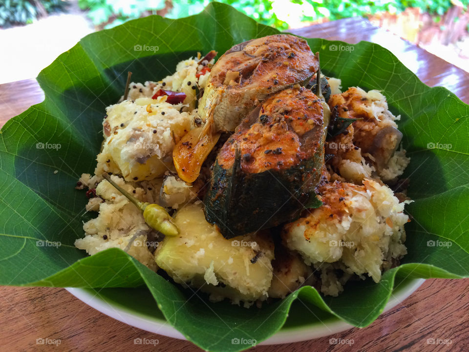 Srilankan style breakfast food plate . boiled and tempered  cassava with spicy fish curry .