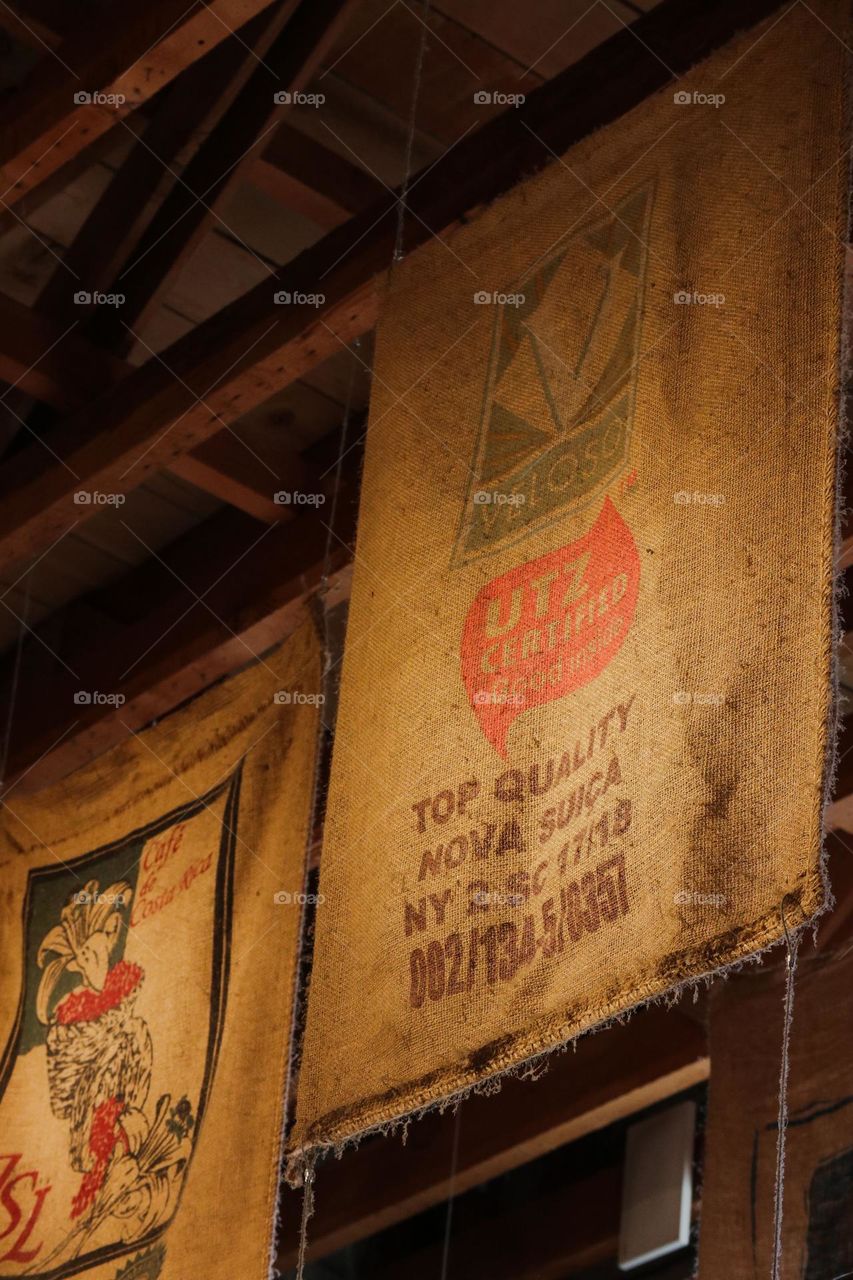 Selection of used burlap sacks that stored coffee from around the world hanging from the ceiling showcasing the diversity of coffee available 