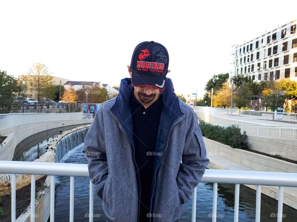 Man standing on bridge over city river at sundown.