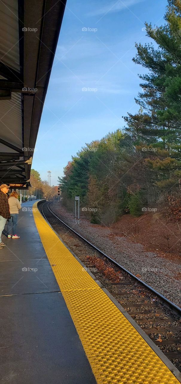 Commuter rail passengers waiting for the train into the City. Sky is blue, a clear day for the train ride.