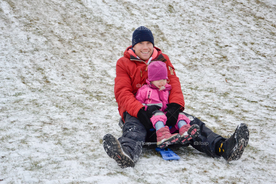 Dad and three year old doughter riding the sledge in the winter.