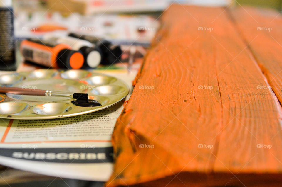 Paintbrush, paint, pallet, and painted wood laid out on newspaper