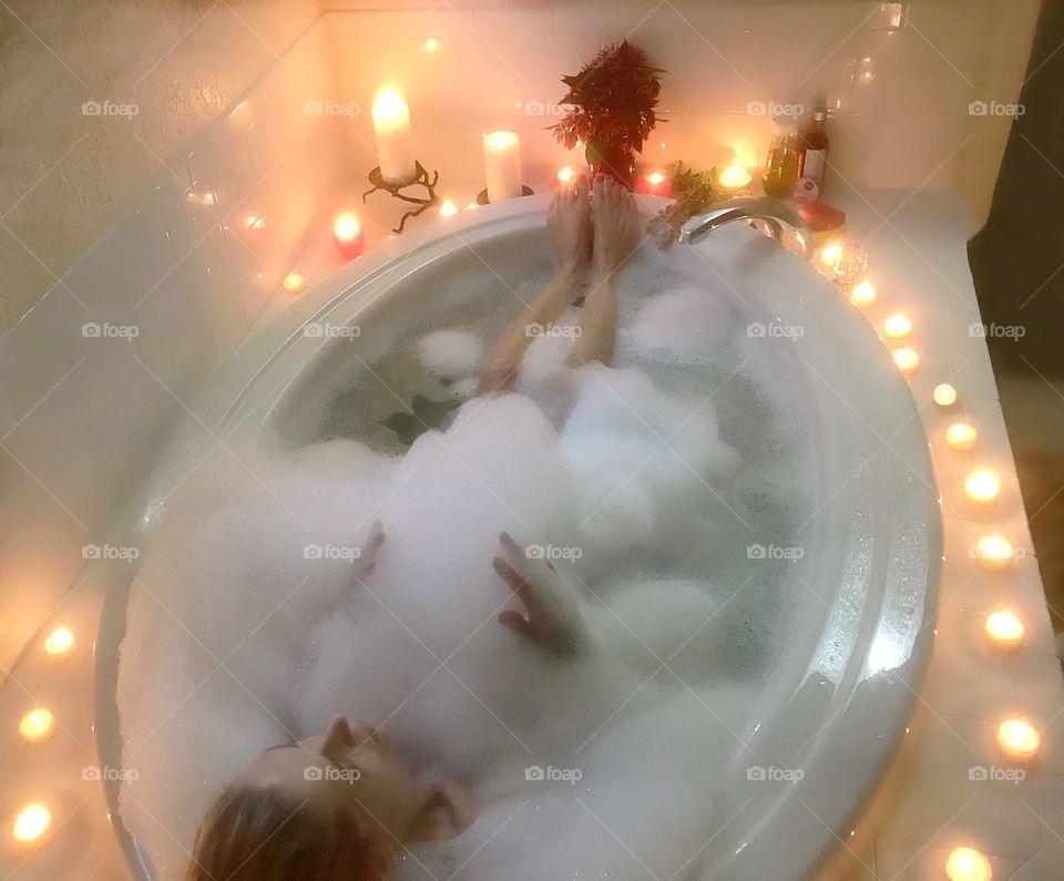A selfie of a woman relaxing in a candlelit luxurious bubble bath.