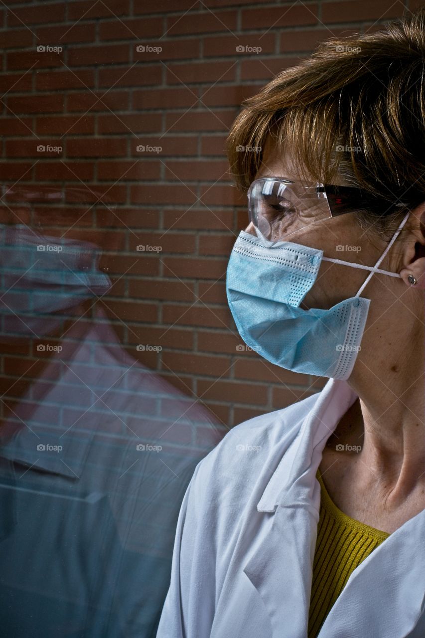 Woman wearing a face mask and protective eyeglasses and looking through the window 