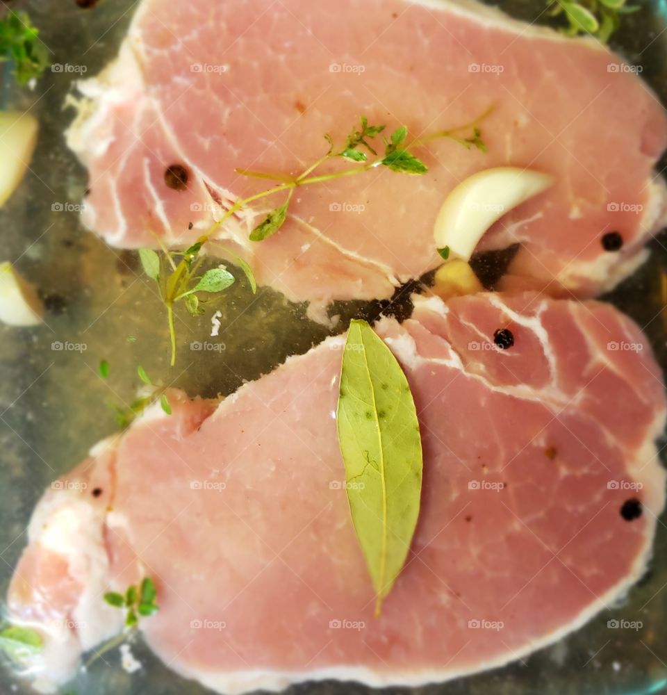 Pork chops marinating with herb leaves and garlic slices.