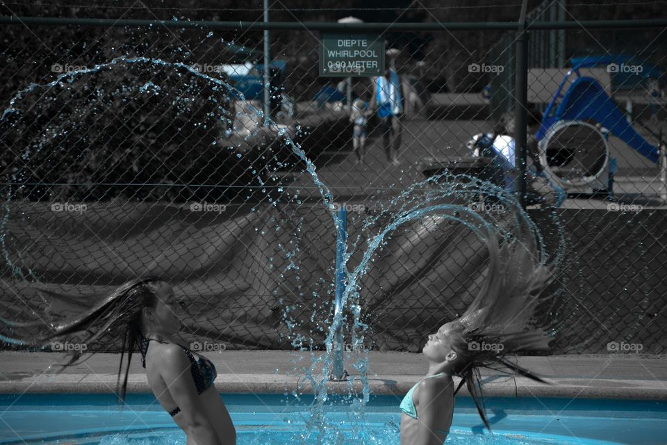 Being playful in the pool and with the camera. Two girls throwing their hair back to create a heart of water 