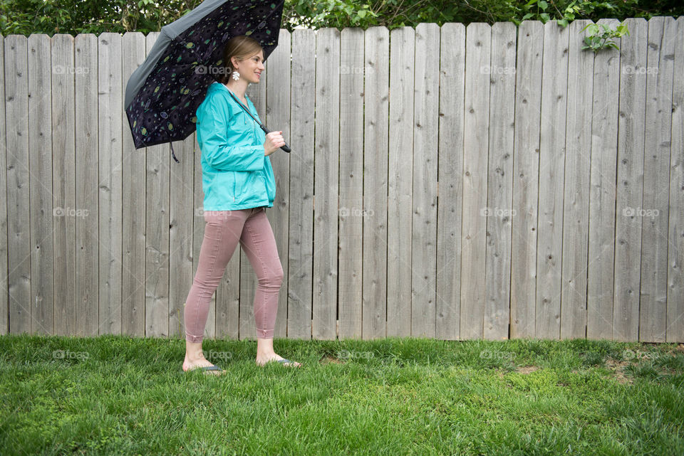 Young woman wearing a raincoat while walking with an umbrella outdoors