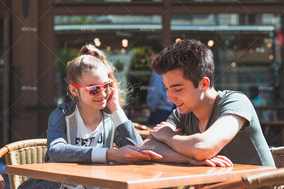 Young woman and man sitting in pavement cafe a the table talking and using mobile phones