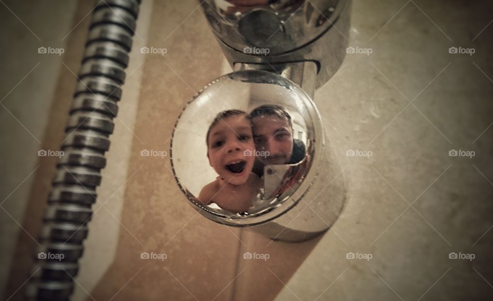 Reflection of father and son on shiny bathtub drain