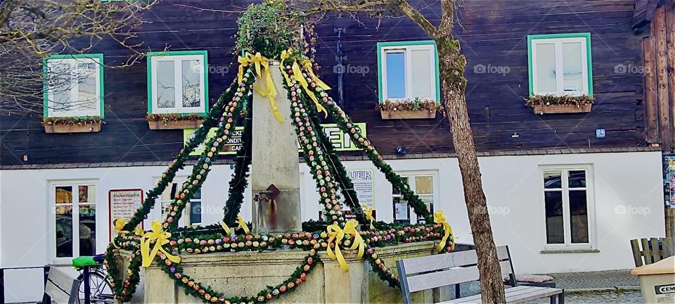 This old well in “Ortenburg”, “Bavaria”, Germany has been festively decorated with plant girlands, ribbons and artificial eggs for “Easter” this Spring. 2024. Hypnotic Productions