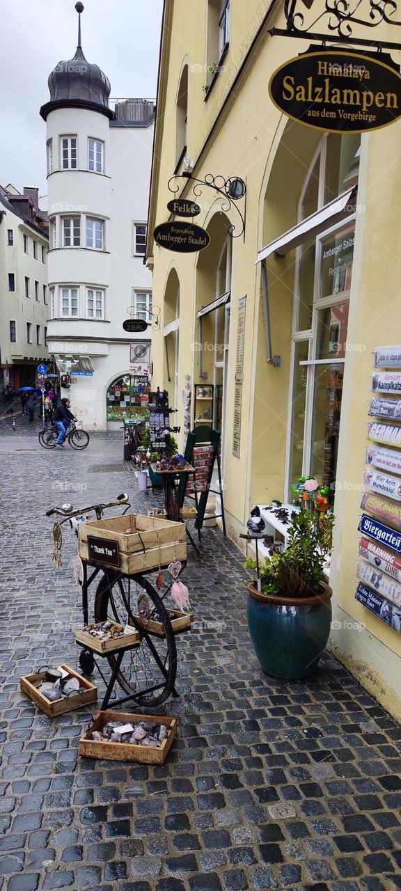 A scenic side street in “Regensburg”, Germany covered entirely with cobblestone features many small shops, cafés and restaurants and space to park bicycles or motorcycles. 2023. Hypnotic Productions