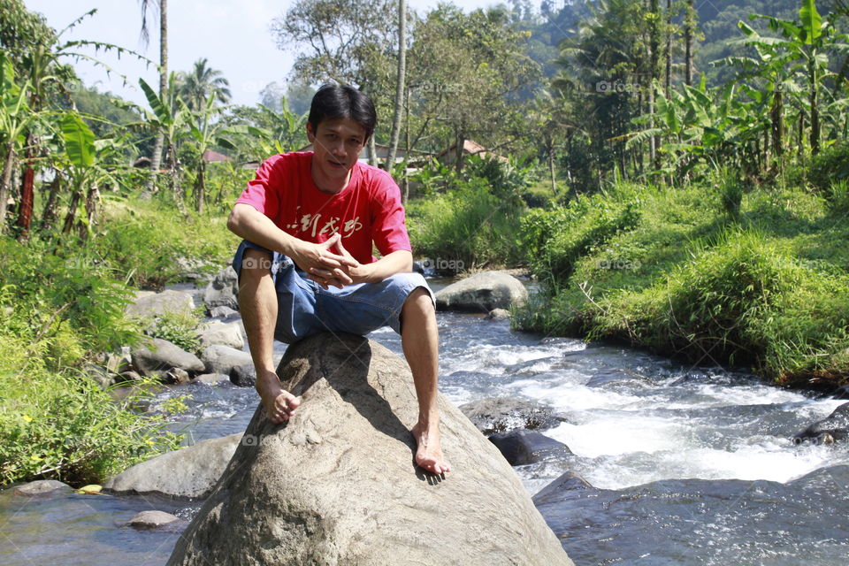 Asian man sitting on rock in the stream