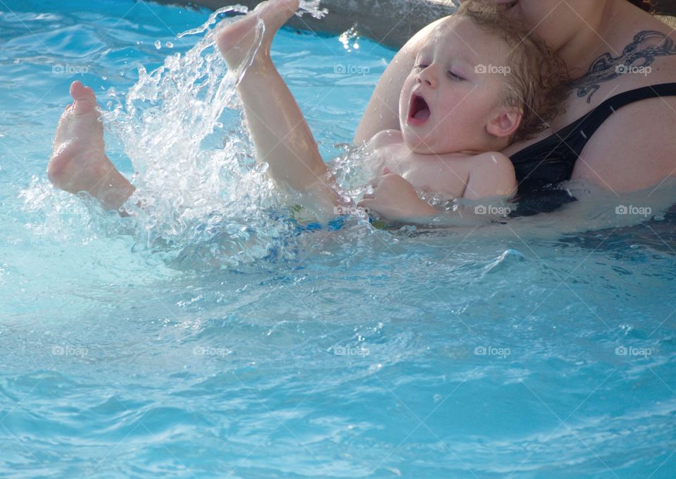 A toddler boy at the outdoor swimming pool for his first round of swimming lessons on a sunny summer evening. 