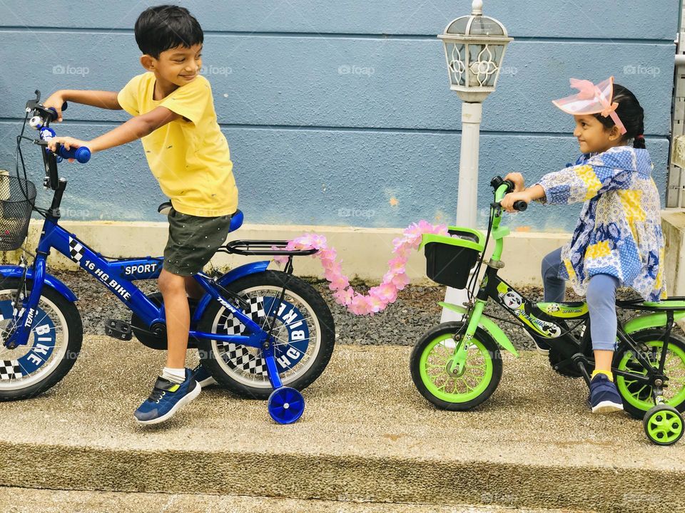 A brother and sister on their bicycles and making fun outside the house 