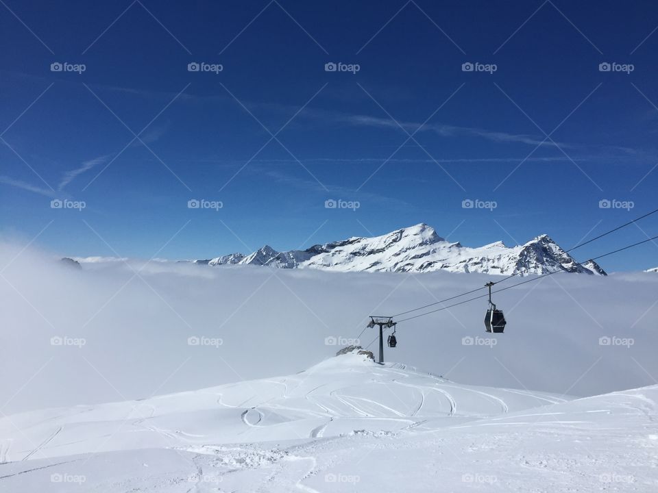 A view of ski lift cabin against blue sky. High in the mountains covered in snow. Italy
