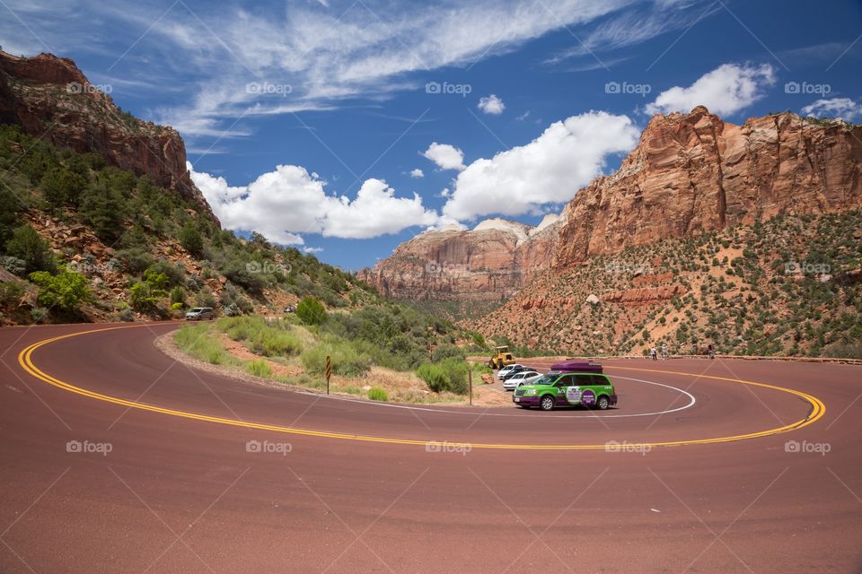 Curvy red road and mountains. Hairpin on red road. Mountain scenery in Zion national park. Cars parked next to the road. People taking photos