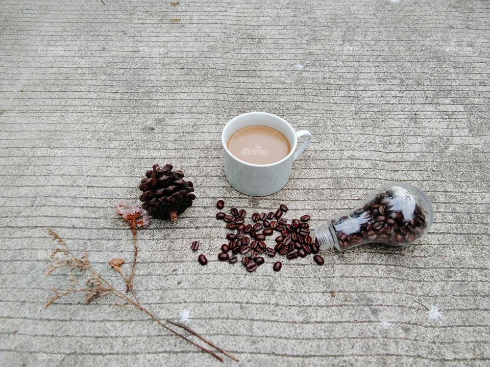 A White cup of coffee and coffee beans in glass bottle on concrete floor