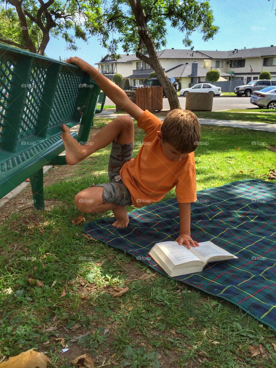 A boy is reading while clinging to the bench. He is immersed in action, very concentrated on what he is reading. 