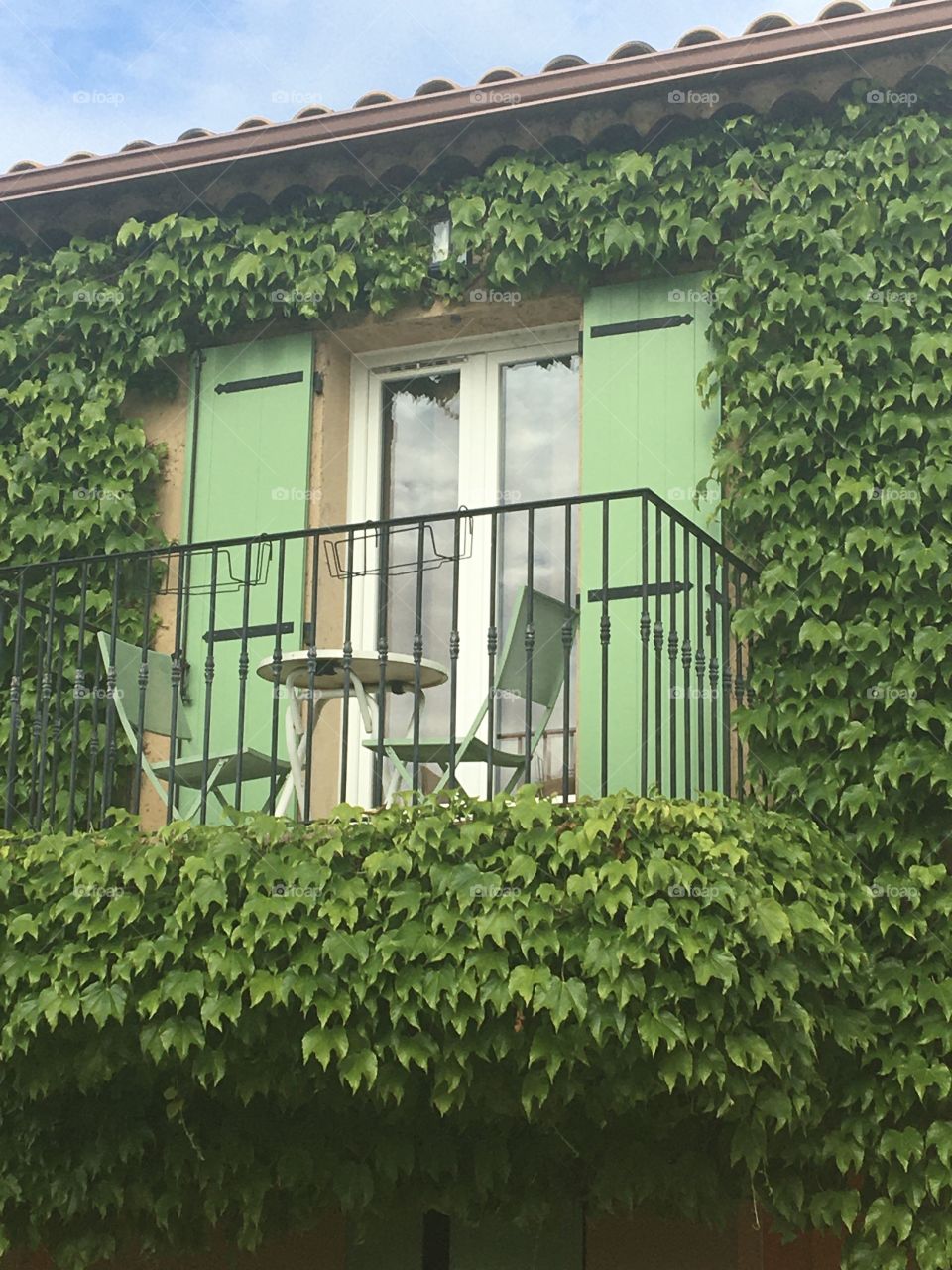 Closed windows on a private balcony all in green reflecting clouds