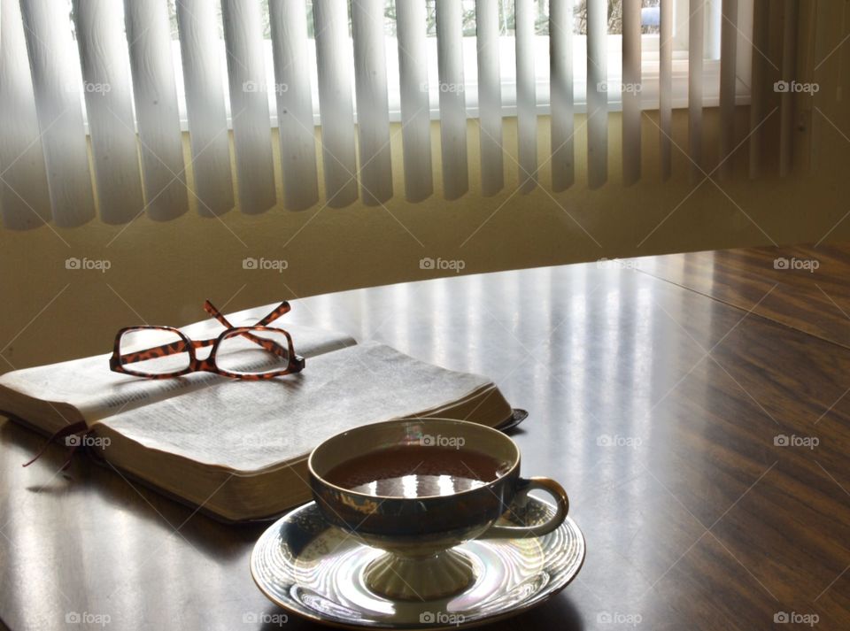 Open Bible with reading glasses sitting on it and a cup of tea beside it