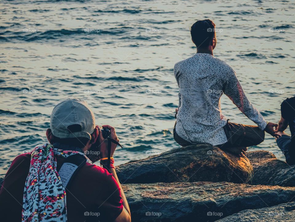 A young man doing meditation in a sea shore and another young man capturing it for small happiness 