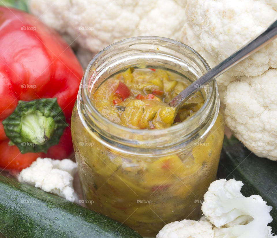 Jar of homemade Mustard Pickles in a surrounded by red capsicum, cauliflower and zucchini.