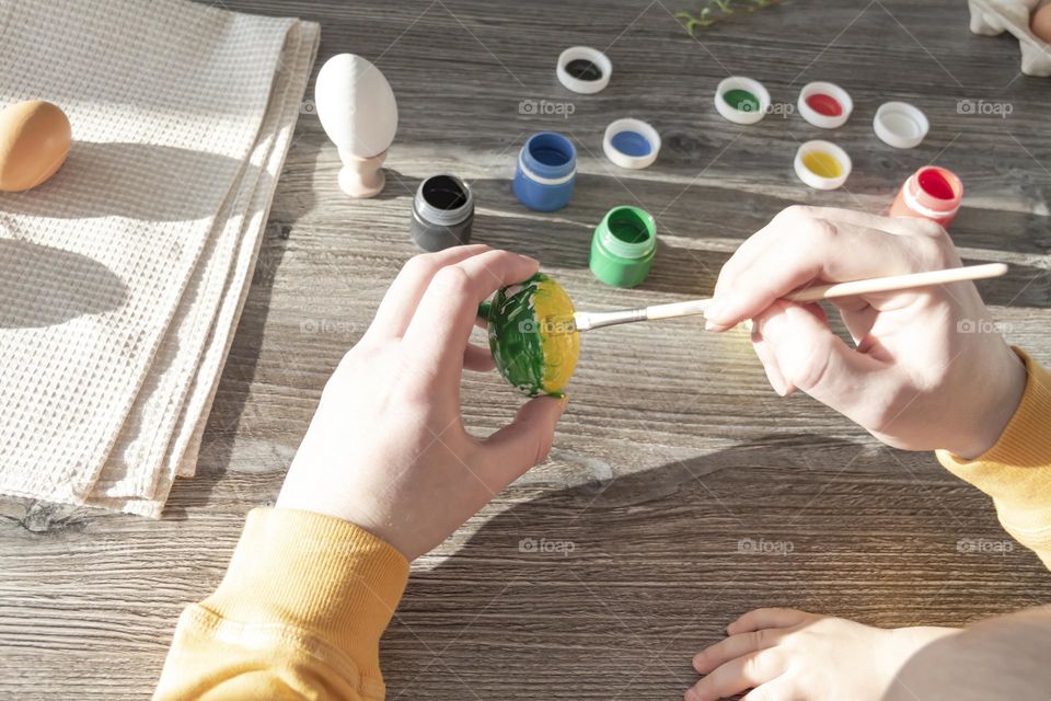 A little son and his father together in their free time paint Easter, chicken eggs with paints and brushes for the holiday. A child and a man create a craft and natural product in their family business.