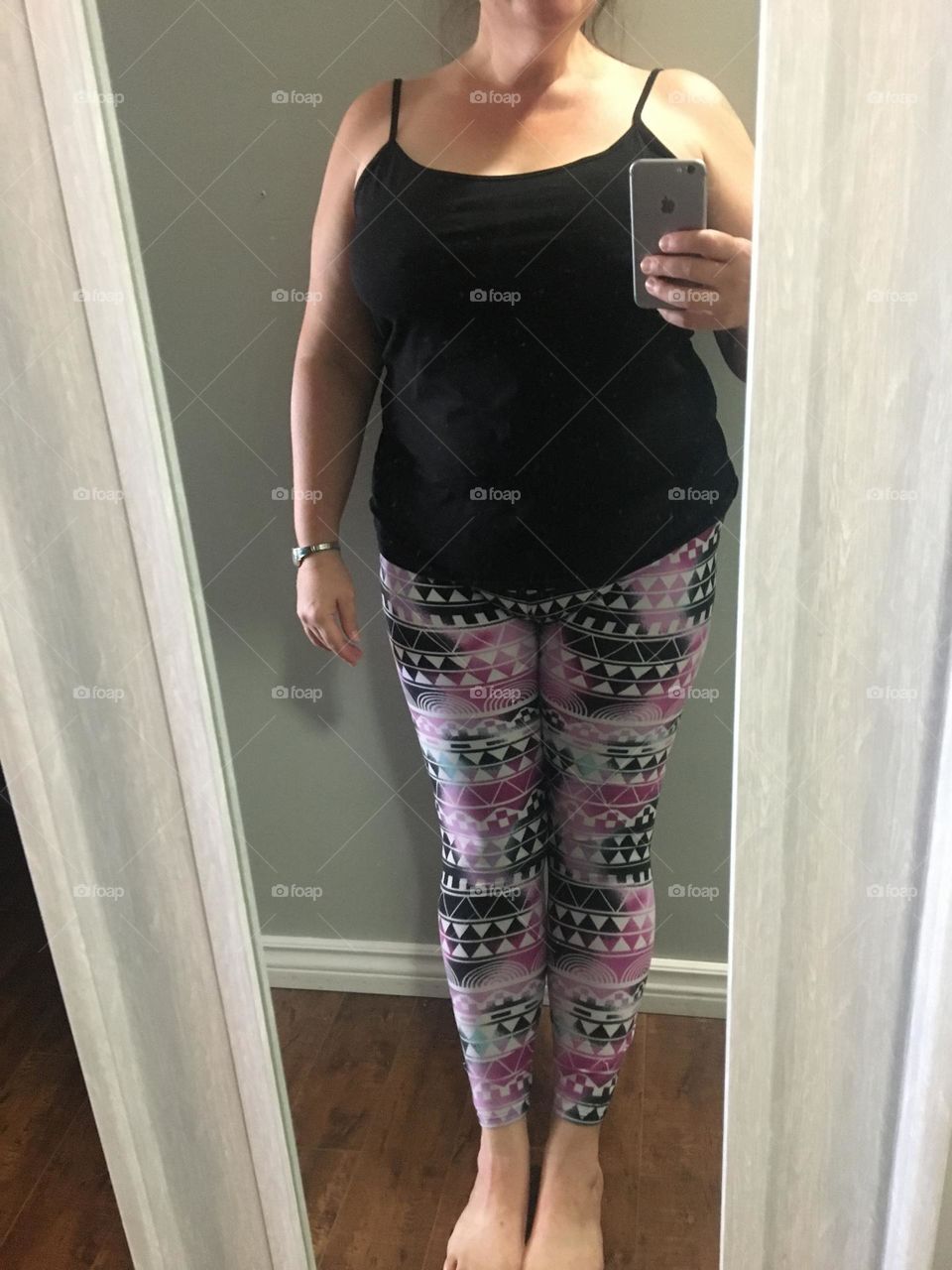 Middle aged plus size lady models her funky, pink, white, black and hint of blue leggings off with her black tank top, in the mirror so she can take a picture with her iPhone