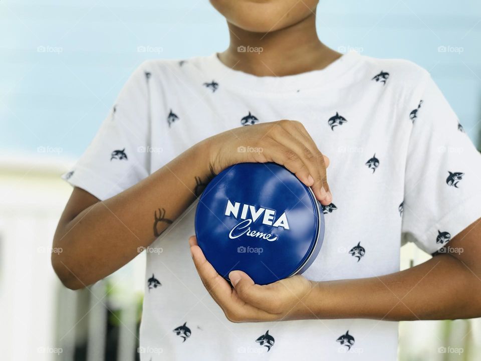 A boy holds Nivea cream with his two hands.