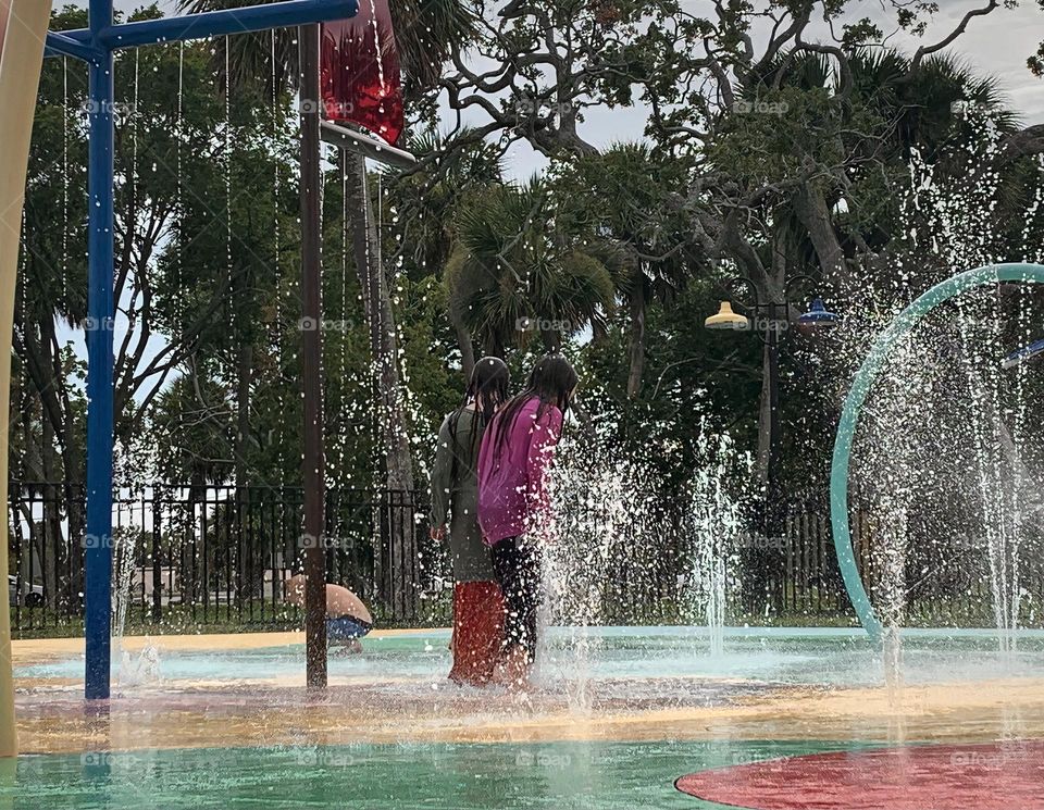 Children having lots of fun in the water at the colorful kids splash pad at the city park for children during a really warm day in Florida.