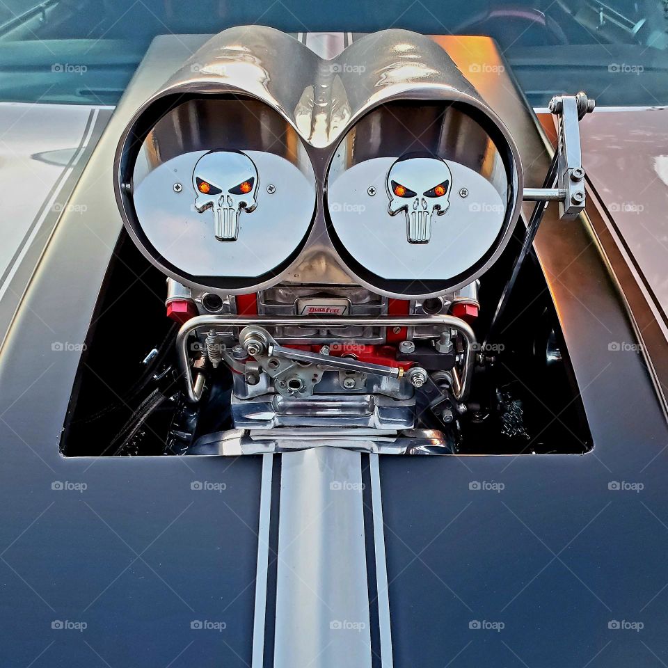 A 1960's classic hot rod has a powerful modified engine with chrome air intakes with the Punisher from comic books