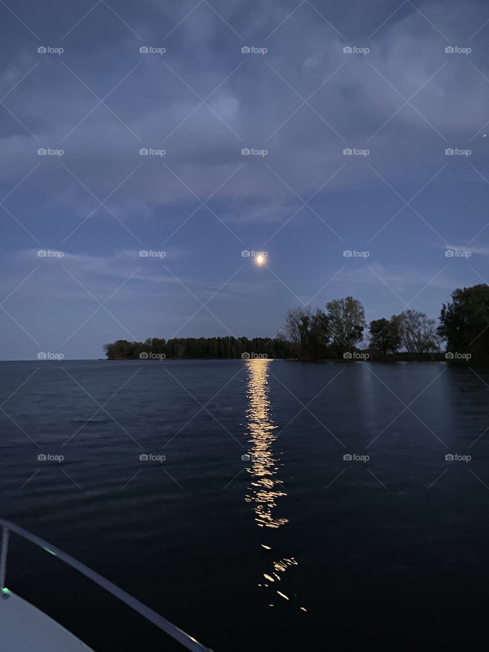 Moonrise over the lake with a deep blue sky and soft clouds. 