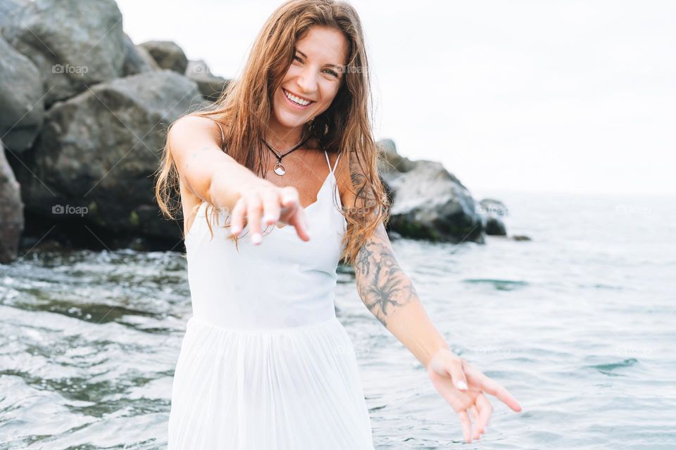 Young carefree beautiful woman with long hair in white dress enjoying life on sea beach