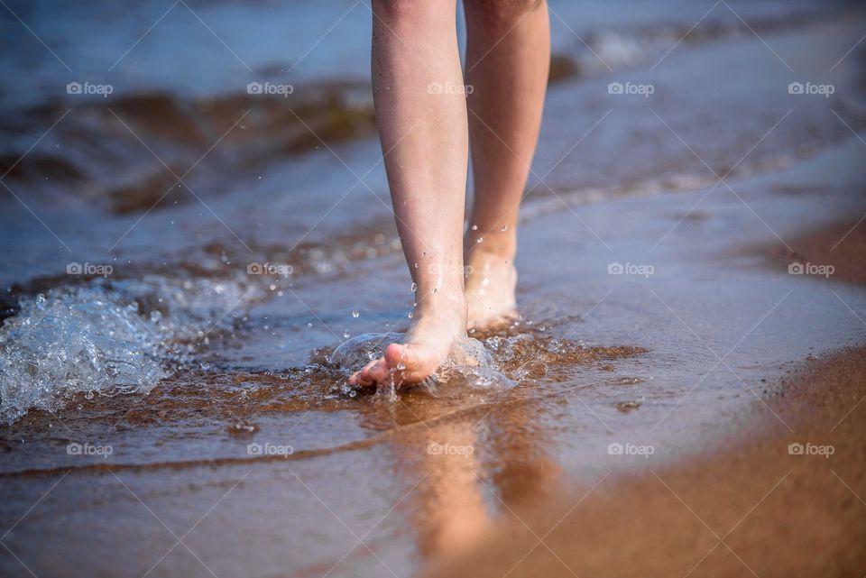 Female feet go on water on the seashore.