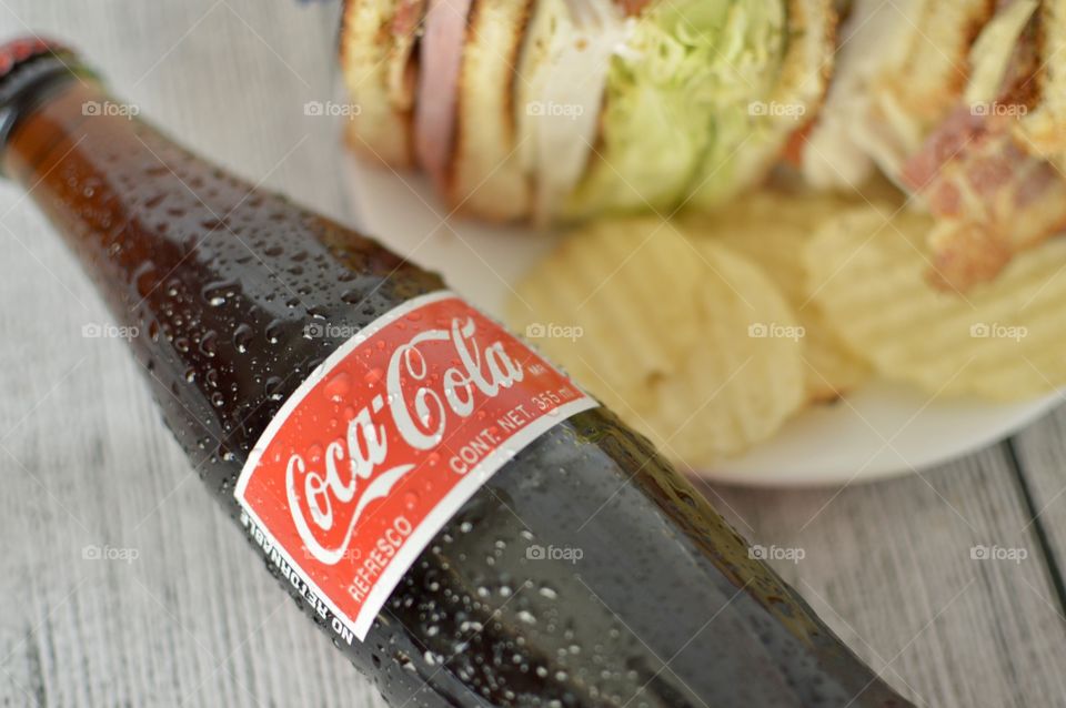 A can and a Bottle of Coca Cola with a club sandwich on a white rustic background 